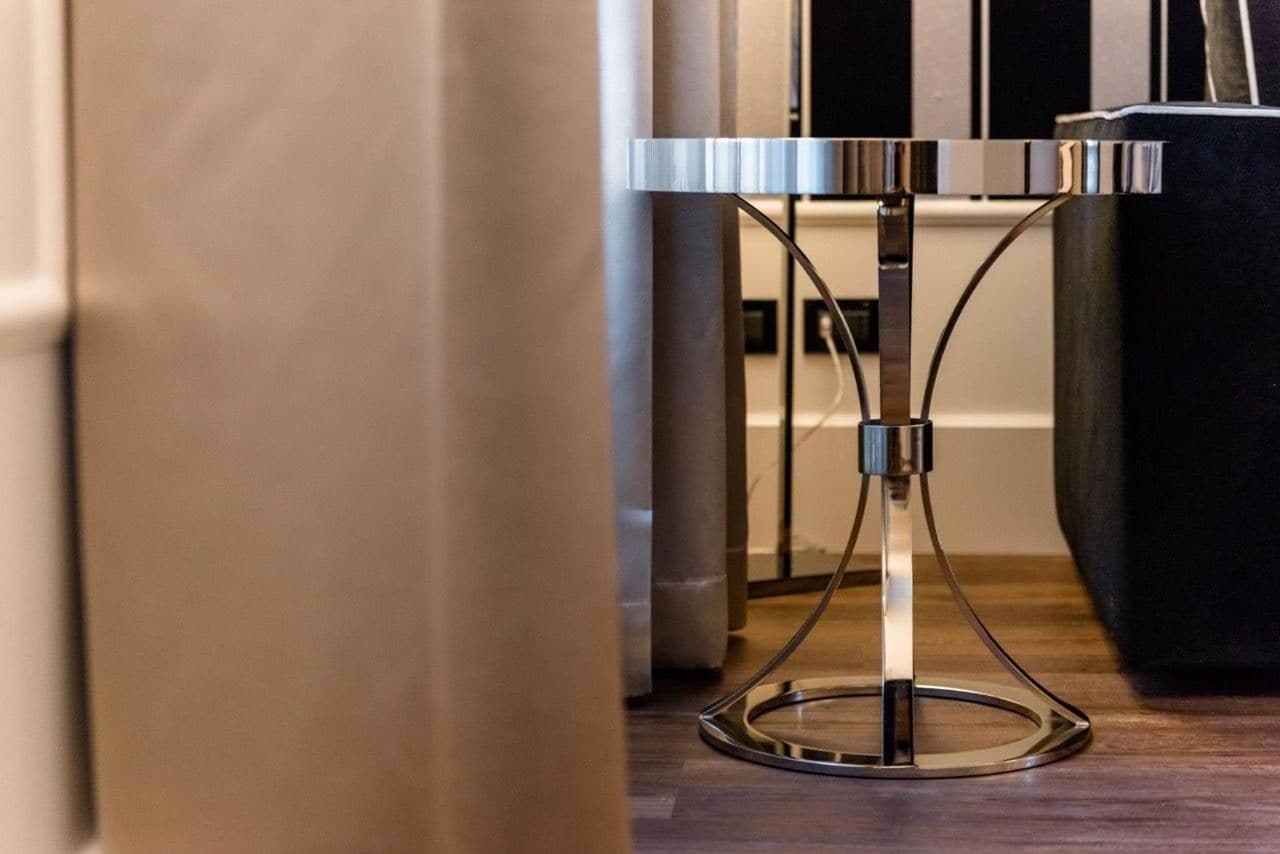 Mesa moderna com estrutura metálica e base circular, situada num espaço com chão de madeira e um pilar grande ao fundo.