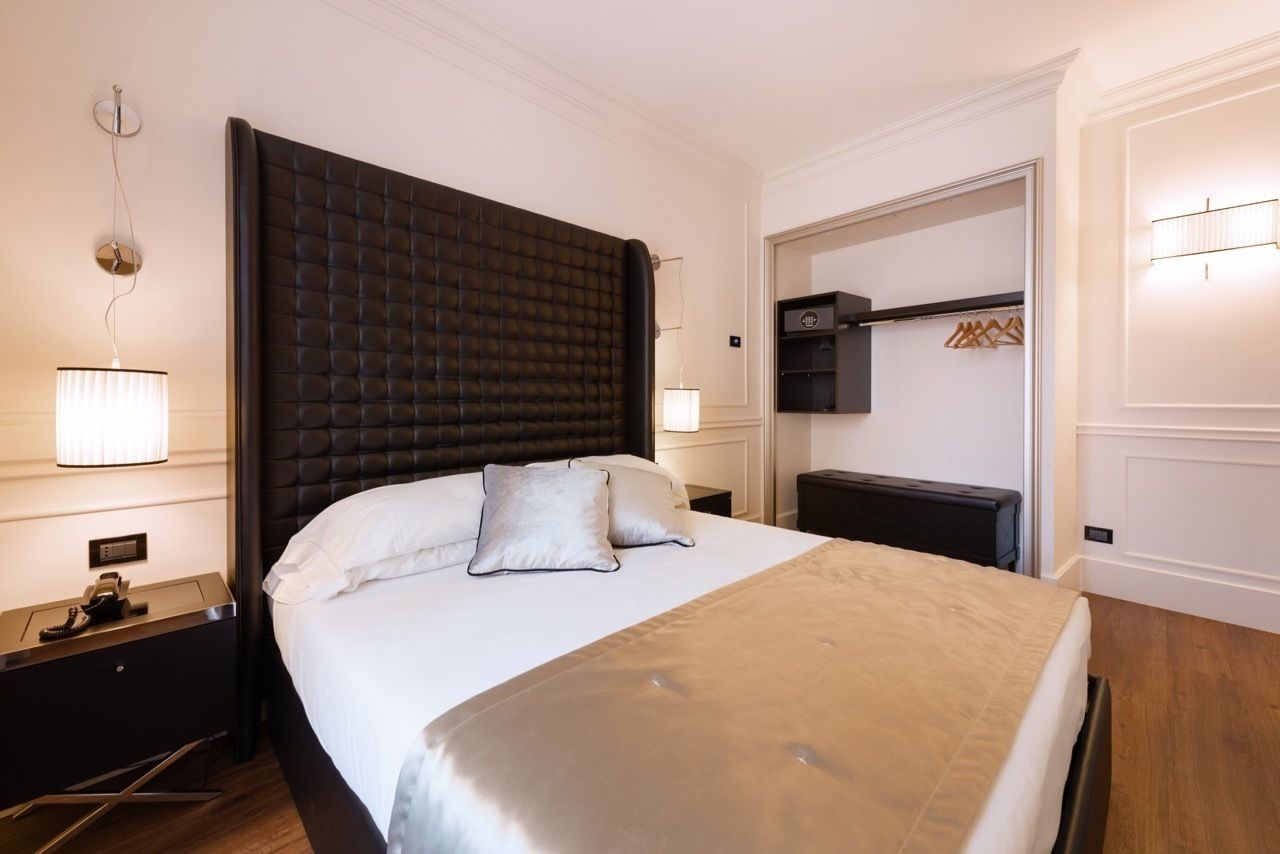 Hotellihuone, jossa on suuri sänky, yöpöytä, lamppu, vaatekaappi ja peili.