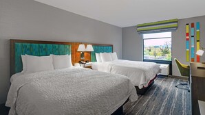 A hotel room with two beds, a desk, a chair, a window with a view, and a colorful wall decoration. - Hampton Inn Utica (Utica)