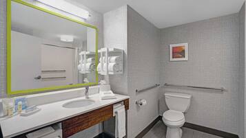 A modern bathroom with a large mirror, white sink, and toilet. There are towels and toiletries on the counter.