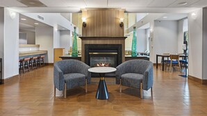 A lobby with a fireplace, two armchairs, a round table, and a bar area with stools.