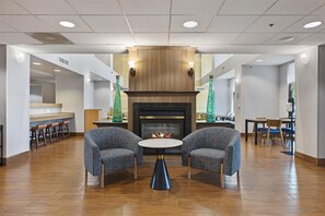 Un hall con chimenea, dos sillones, una mesa redonda y una zona de bar con taburetes.
