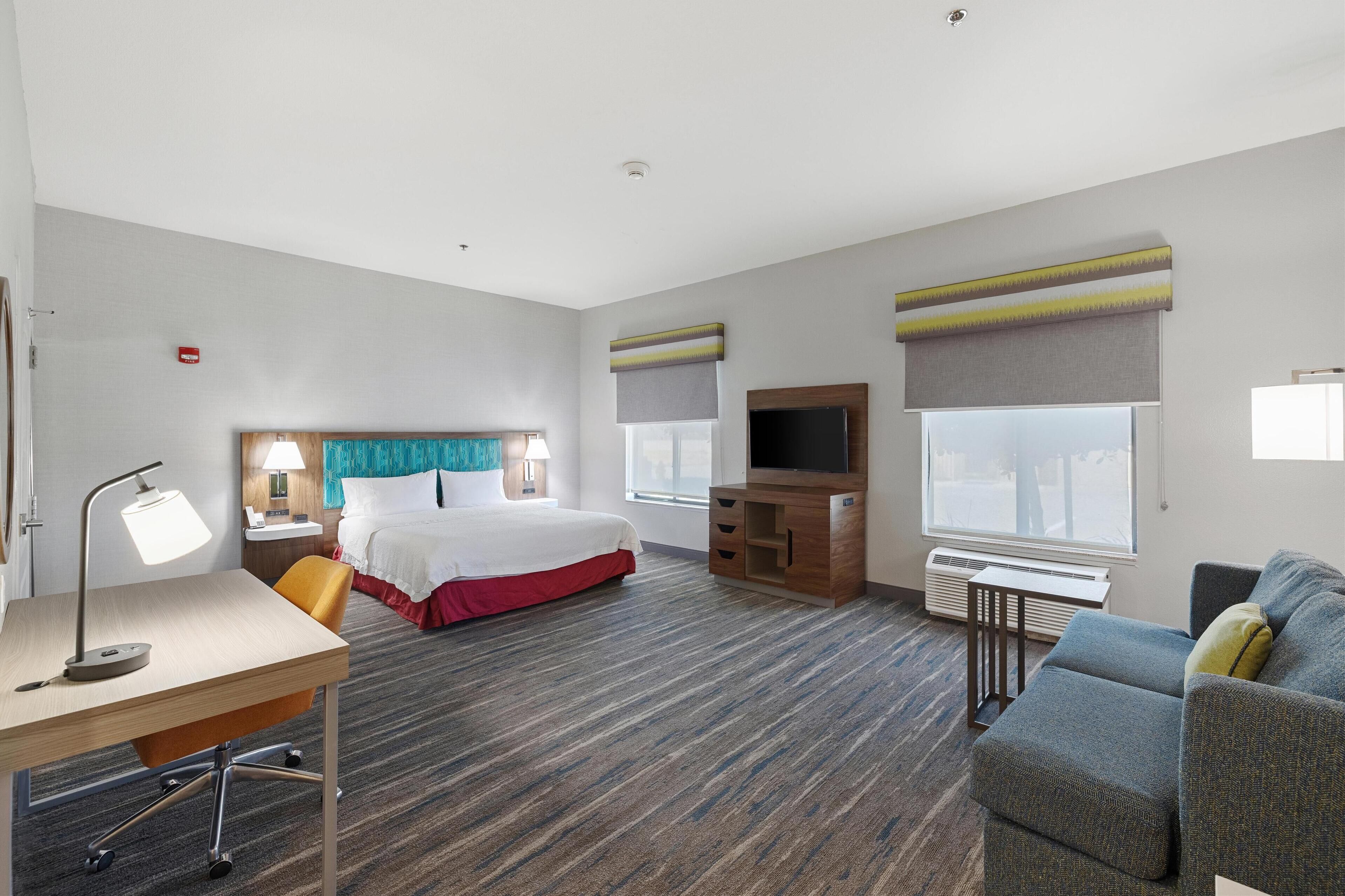 A hotel room with a bed, desk, chair, TV, and sofa.