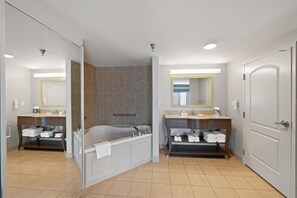 Un baño moderno con bañera, dos lavamanos, ducha y zona de ducha con mampara de cristal.