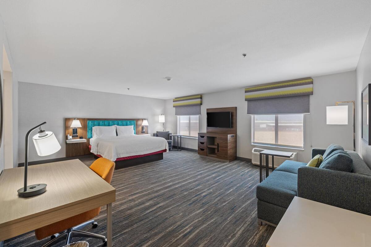 A hotel room with a bed, desk, chair, sofa, TV, and windows.