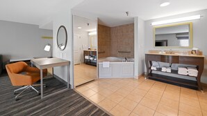 A hotel room with a desk, chair, bathroom with a bathtub, and a vanity with towels.