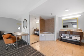 A hotel room with a desk, chair, bathroom with a bathtub, and a vanity with towels.