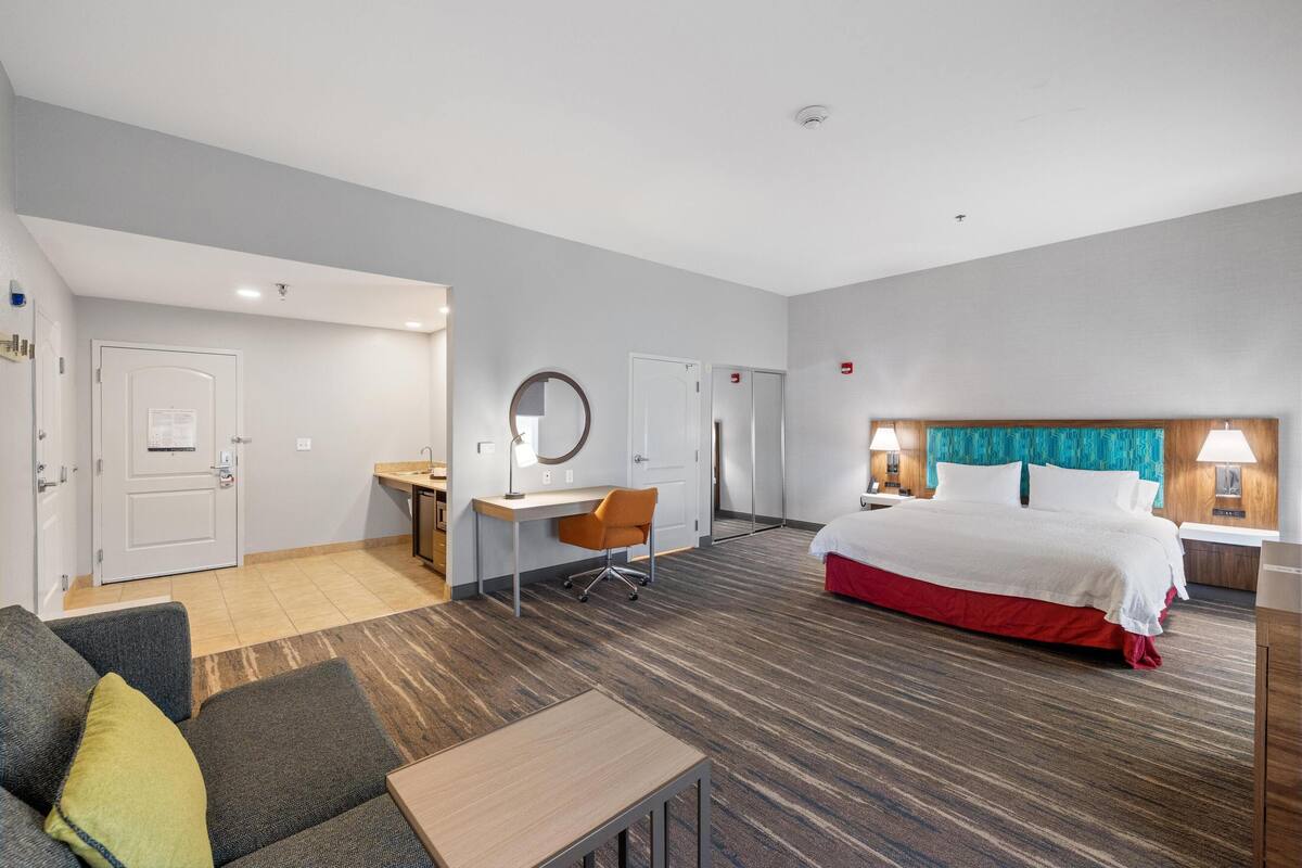 A hotel room with a bed, desk, chair, and a small table.
