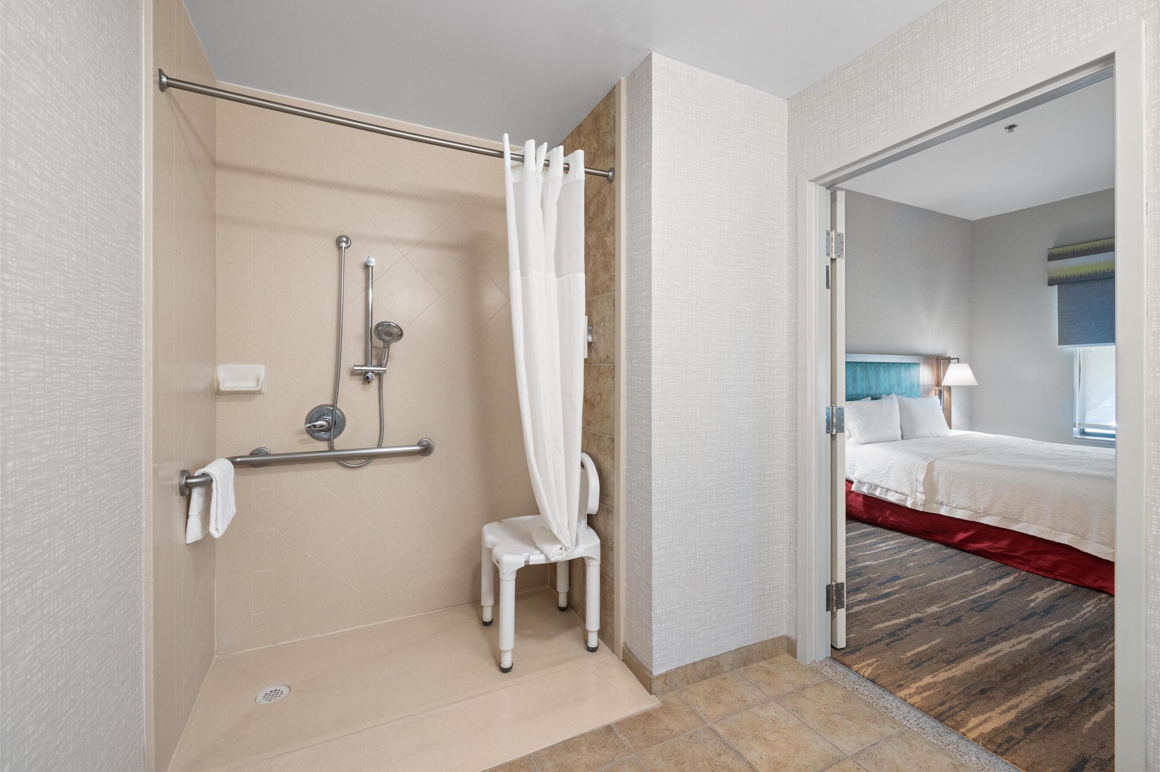 A modern bathroom with a shower, grab bar, and a wheelchair-accessible chair.
