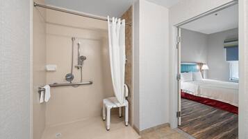 A modern bathroom with a shower, grab bar, and a wheelchair-accessible chair.