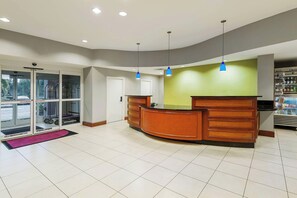 A reception area with a wooden reception desk, glass doors leading outside, and a green wall. - Residence Inn by Marriott Orlando Airport (Orlando)