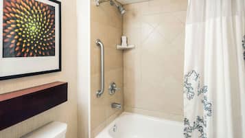A bathroom with a bathtub, a shower, a toilet, a handrail, and a framed artwork on the wall.