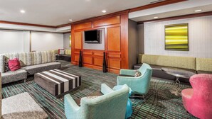 Un moderno vestíbulo de hotel con sofá, sillones, una mesita de centro y un televisor instalado en una pared de paneles de madera.