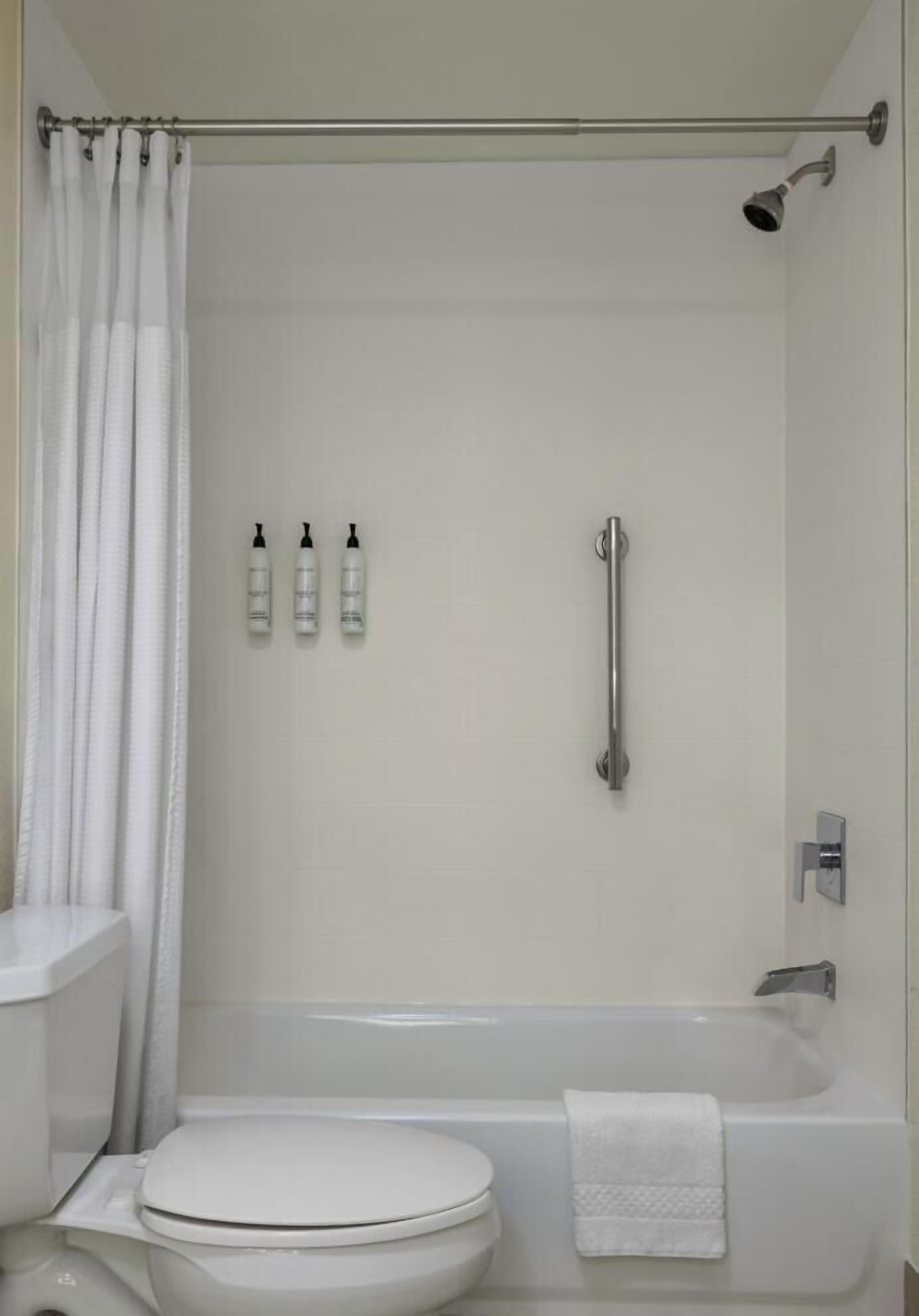 A bathroom with a toilet, a bathtub, a shower, and a handrail.