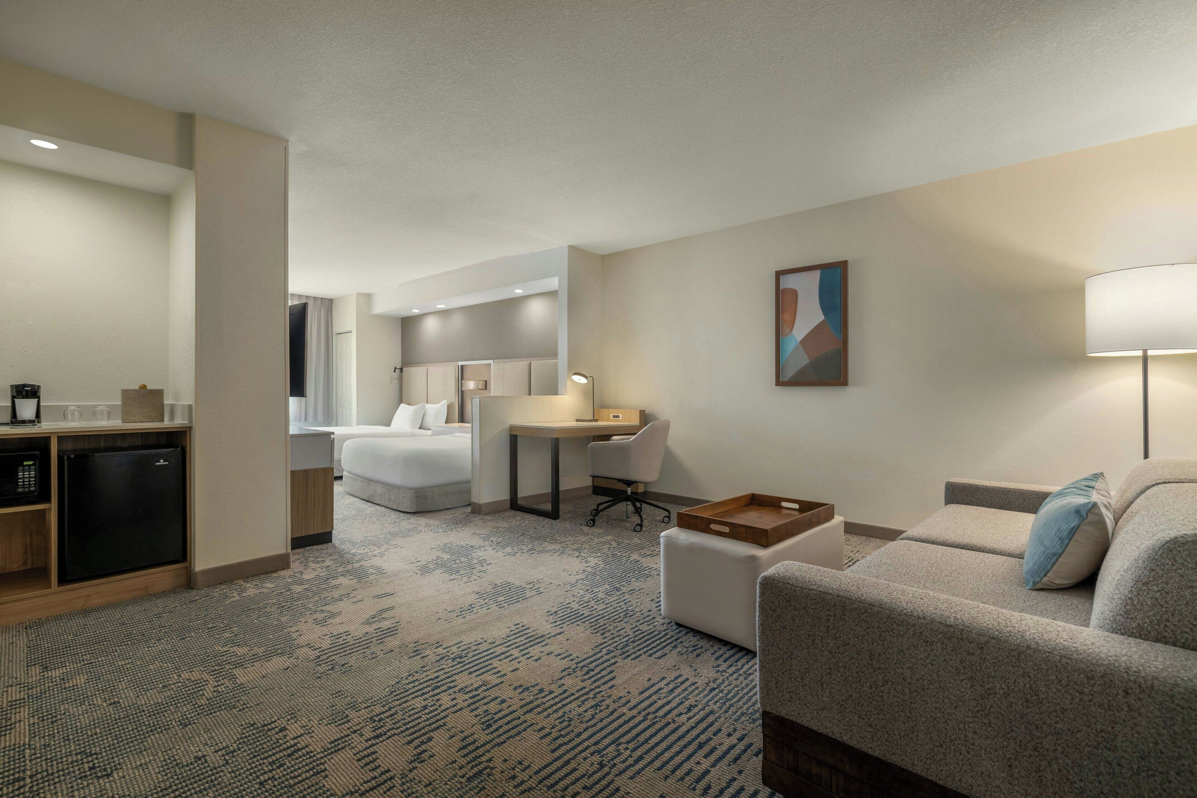 Habitación de hotel con cama, escritorio, silla, sofá, lámpara y una pequeña mesa.