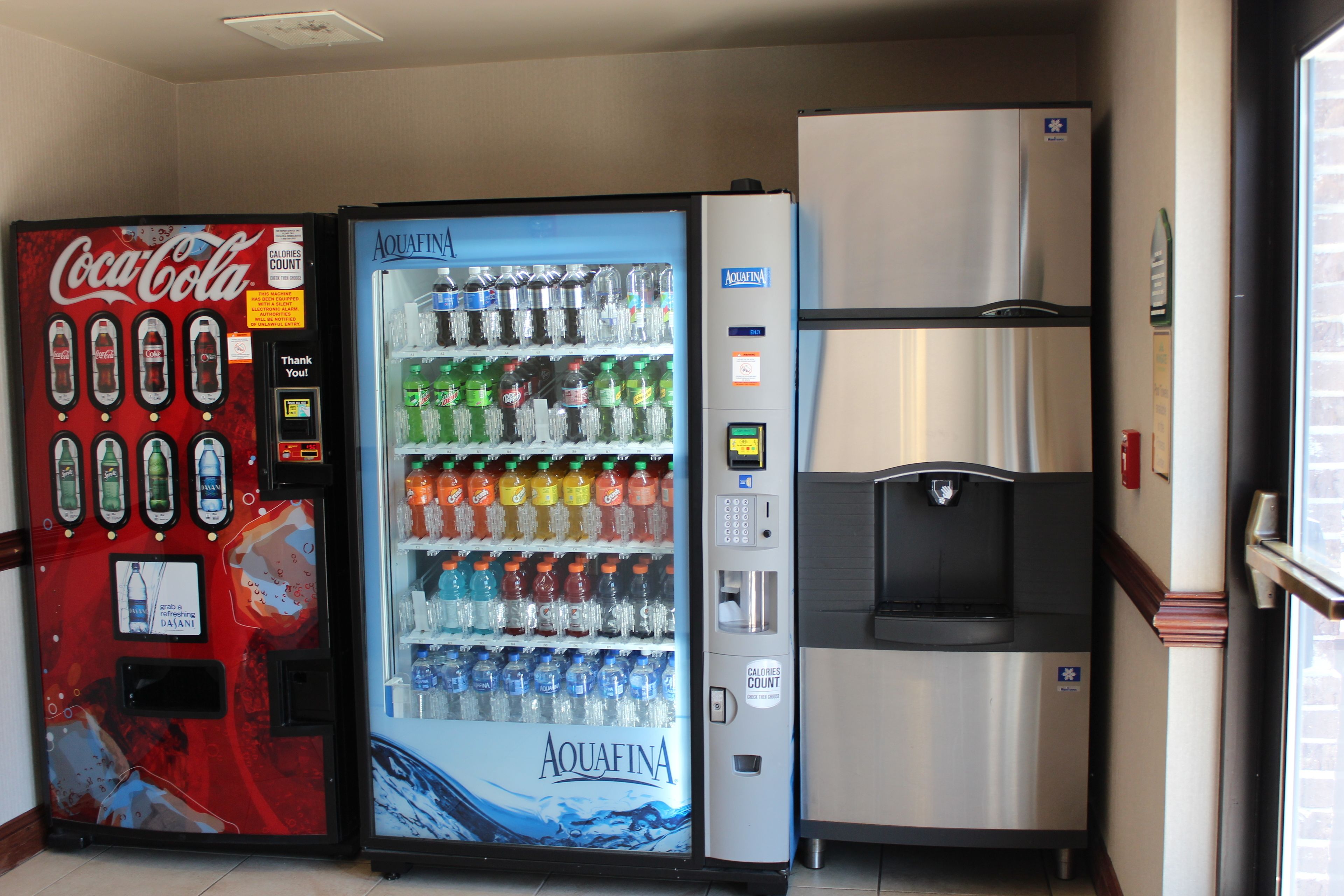 Un área de máquinas expendedoras con dispensador de Coca-Cola y agua Aquafina, y un refrigerador.