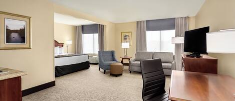 A hotel room with a bed, a desk, a chair, a sofa, a small table, and a television.