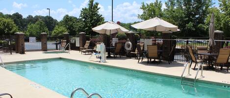 A swimming pool with lounge chairs and umbrellas, surrounded by a brick wall and trees.