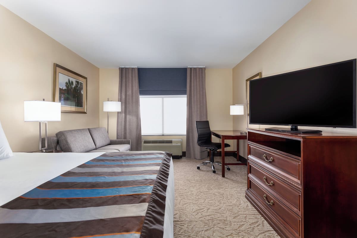 Une chambre d’hôtel avec un lit, un bureau, une télévision et une fenêtre avec des rideaux.