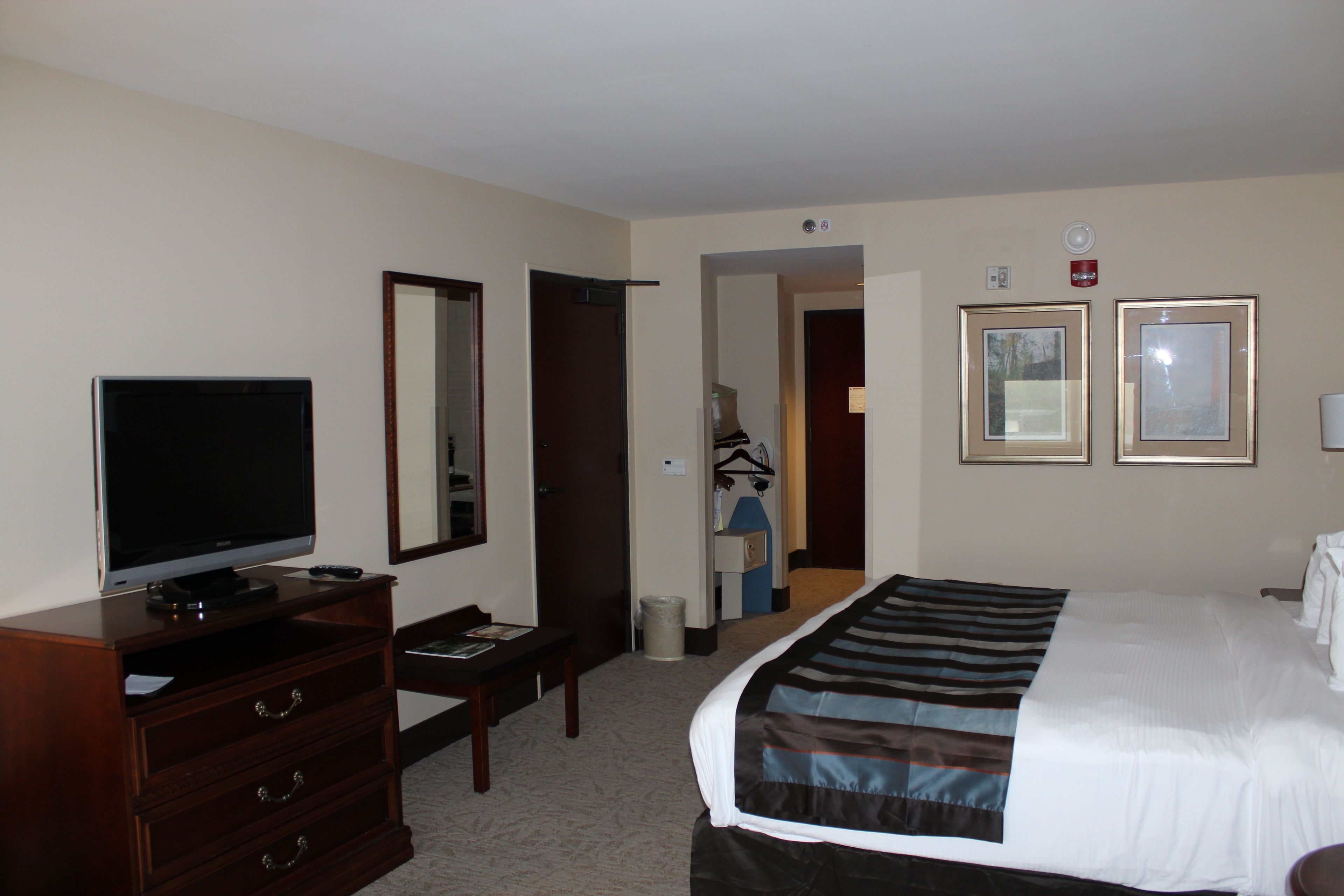 A hotel room with a bed, a TV, a dresser, a mirror, and two framed pictures on the wall.