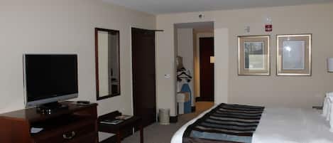 A hotel room with a bed, a TV, a dresser, a mirror, and two framed pictures on the wall.