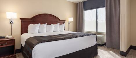 A hotel room with a large bed, two bedside lamps, a nightstand, a window with curtains, and a thermostat.