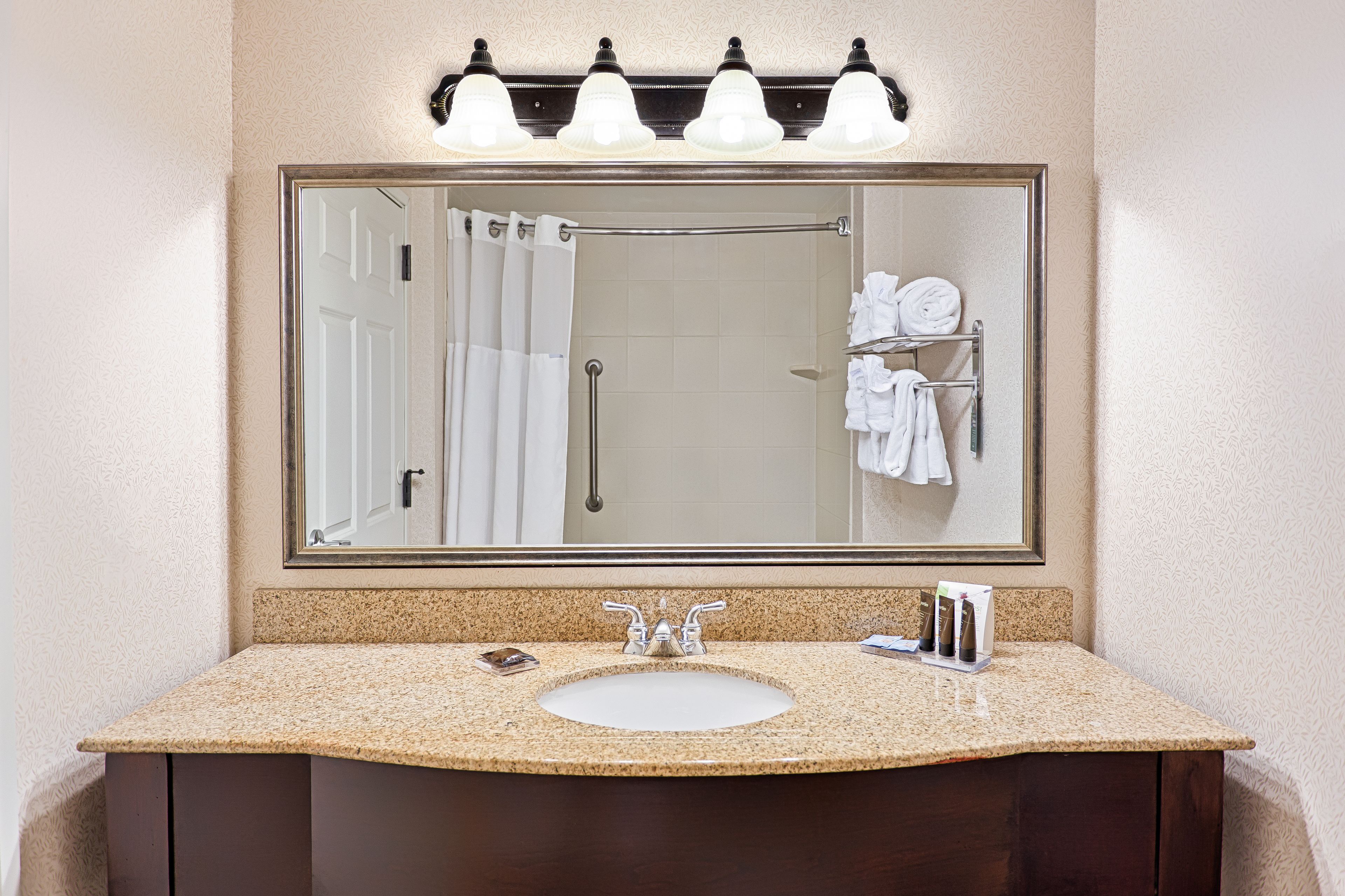 A bathroom with a large mirror, a sink, and a towel rack with towels.