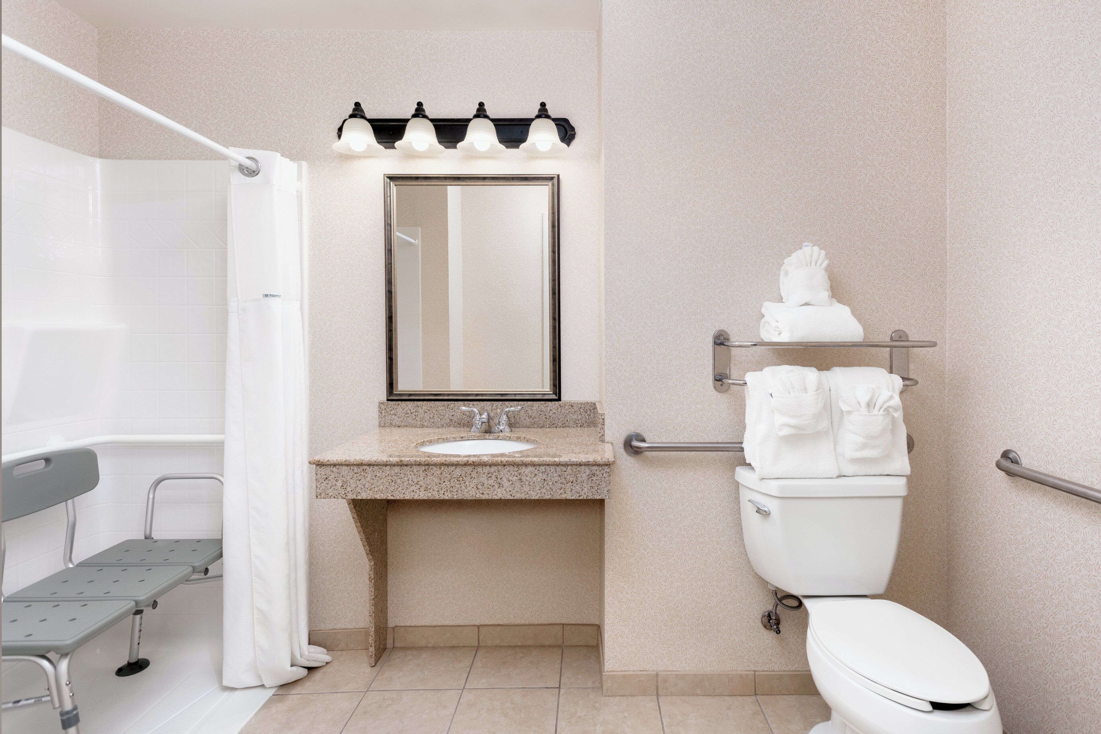 A bathroom with a shower, a sink, a toilet, and a bench.