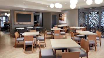 Un comedor moderno con mesas y sillas de madera, una gran pizarra en la pared y un biombo decorativo con patrones geométricos.