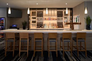 Eine Bar mit einer langen Theke, mehreren Barhocker, einem an der Wand befestigten Fernseher und Regalen voller Flaschen und Gläsern.