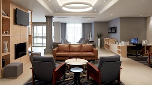 A modern living room with a leather sofa, two armchairs, a coffee table, and a TV mounted on the wall. - Fairfield Inn & Suites by Marriott Montreal Airport (Dorval)