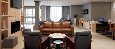 A modern living room with a leather sofa, two armchairs, a coffee table, and a TV mounted on the wall.