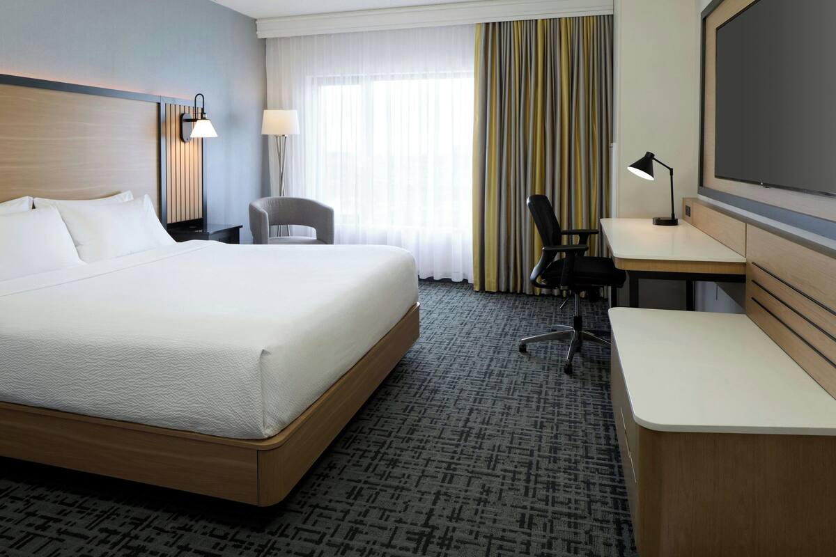 Habitación de hotel con una cama grande, un escritorio, una silla, un televisor y una ventana con cortinas.