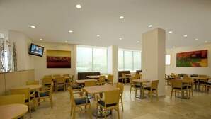 Un comedor amplio con varias mesas y sillas, ventanas grandes y obras de arte en las paredes.