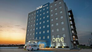 Un hotel de varios pisos con un cartel llamativo que dice 'one hotel', una furgoneta estacionada al frente y un cielo despejado.