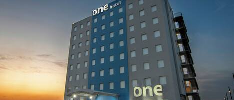 A multi-story hotel with a prominent 'one hotel' sign, a van parked in front, and a clear sky.