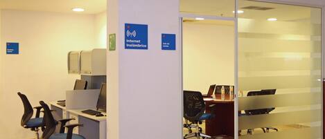 Un espacio de oficina con cubículos, computadoras y sillas de escritorio. Se observan carteles que indican acceso a Internet y una sala de reuniones.