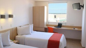 Habitación de hotel con dos camas, un escritorio, un televisor y ventana con vistas.