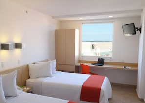 Habitación de hotel con dos camas, un escritorio, un televisor y ventana con vistas.