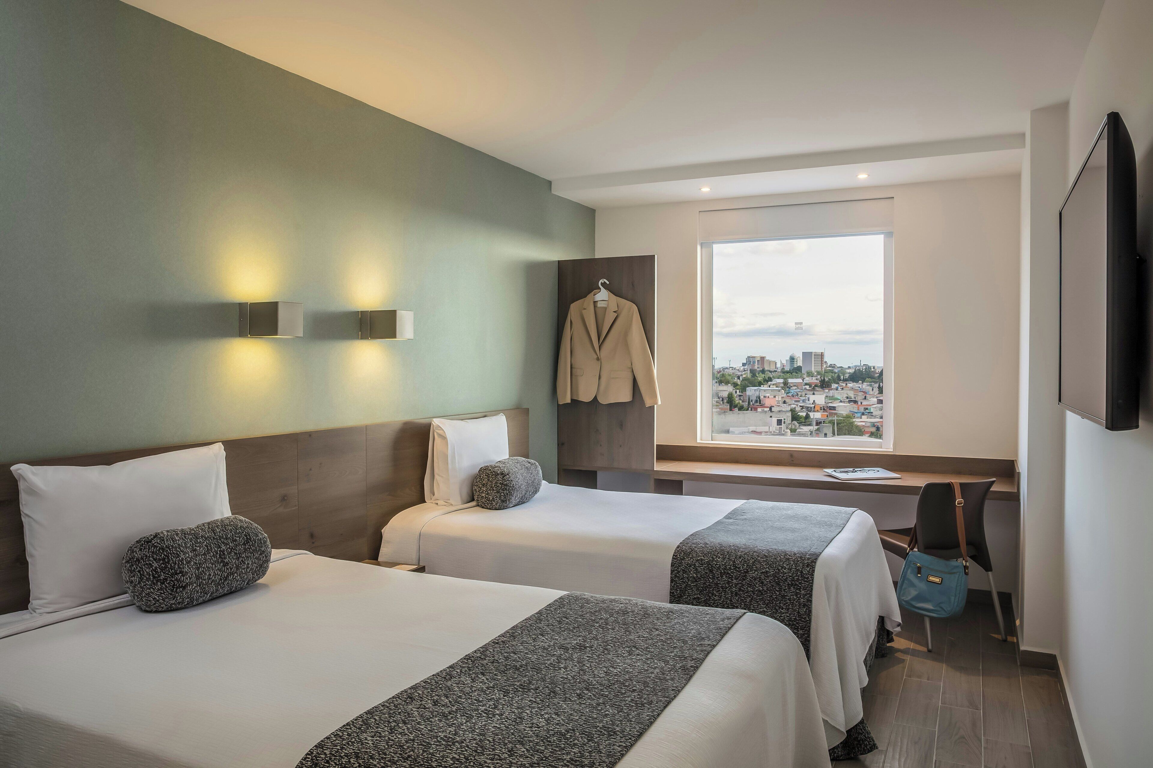 Une chambre d’hôtel avec deux lits, une vue sur la ville, un porte-manteau, un bureau et une télévision.