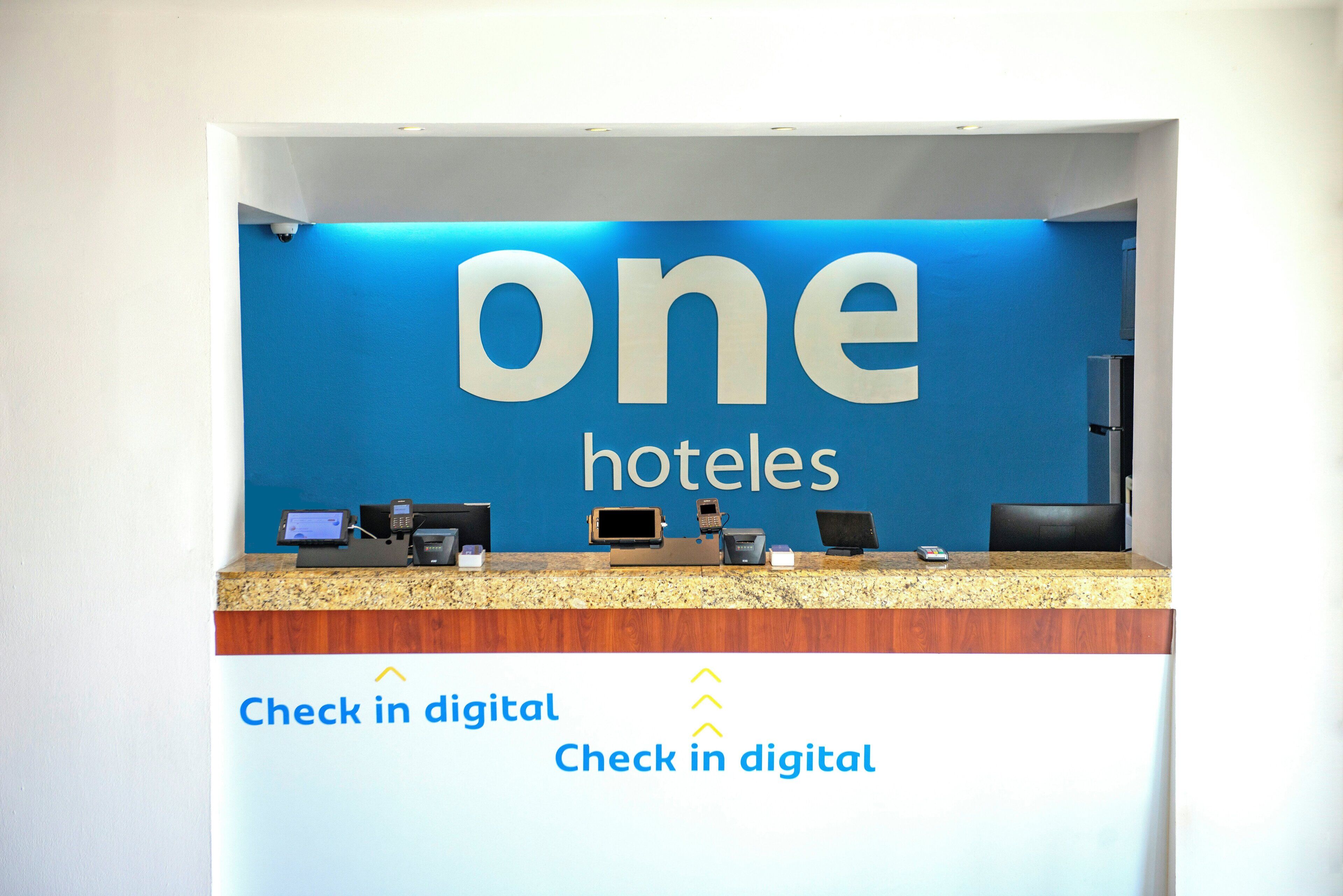 A reception desk with a digital check-in system and a sign reading 'one hotels'.