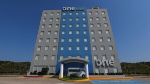 Un hotel con fachada azul y gris, una entrada central con toldo, y una furgoneta estacionada frente a él.