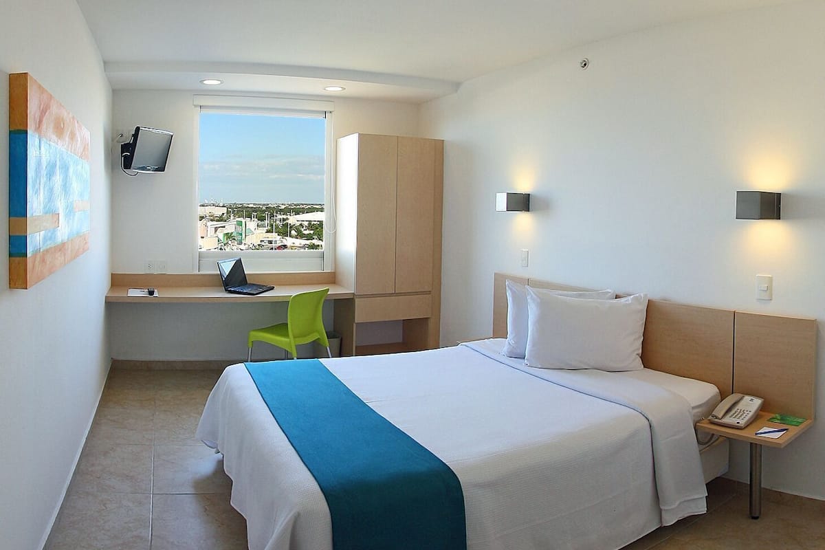 Habitación de hotel con cama, escritorio, silla y vistas a la ciudad.