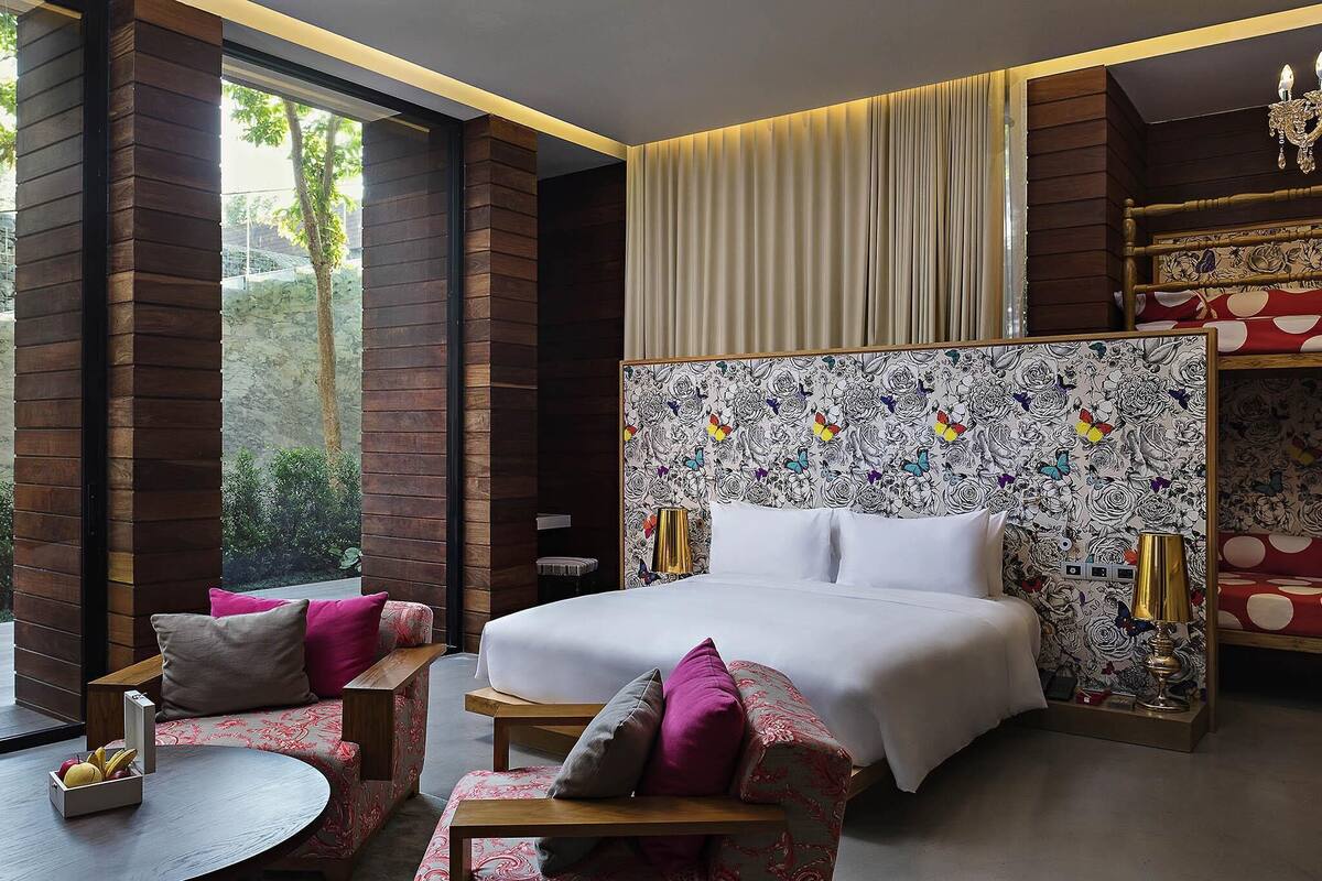 Een moderne hotelkamer met een groot bed, twee stoelen, een klein tafeltje en een decoratief hoofdbord.