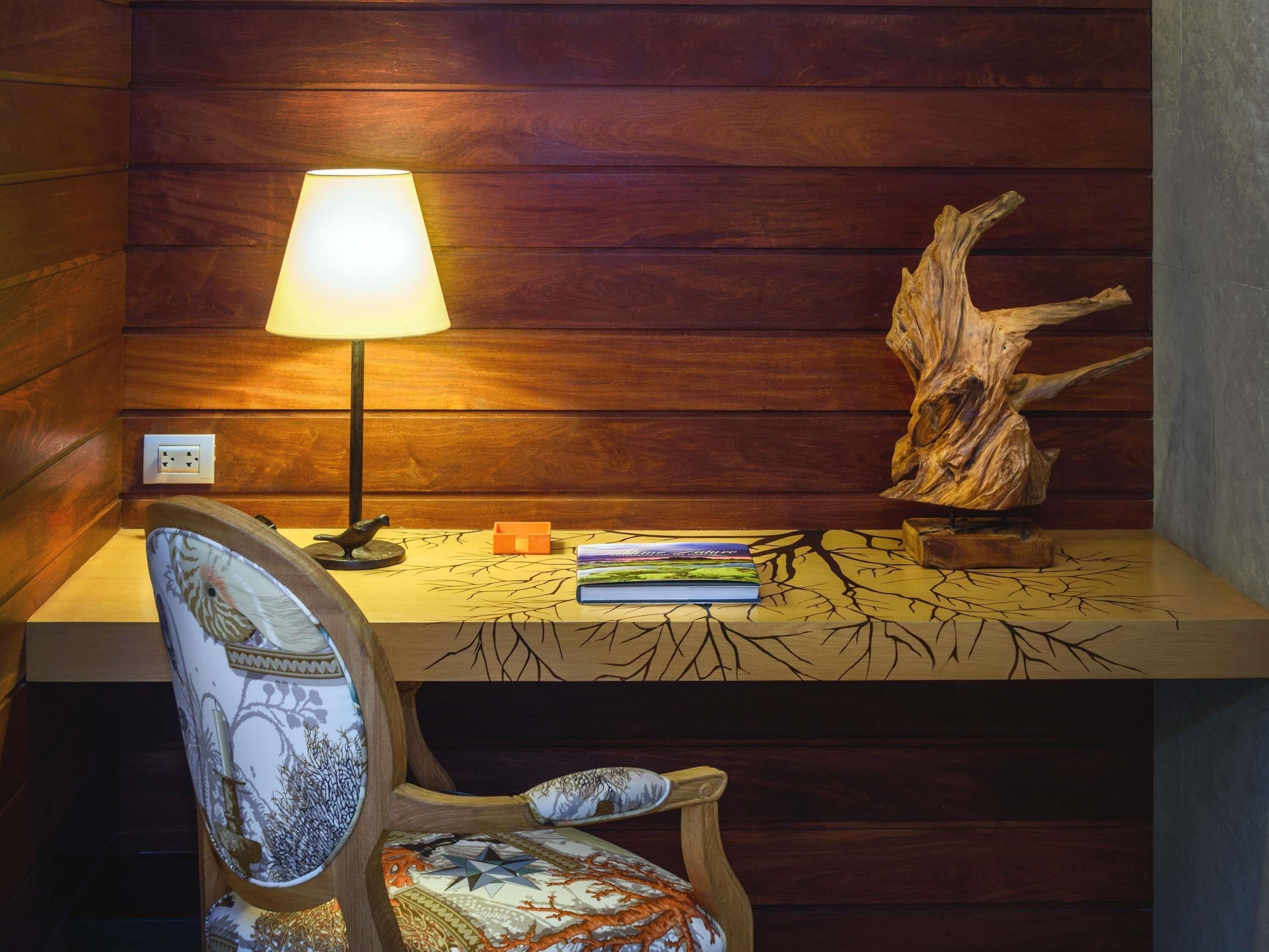 Een houten bureau met een lamp, een stoel met een gestreept kussen en een decoratieve boomstam.