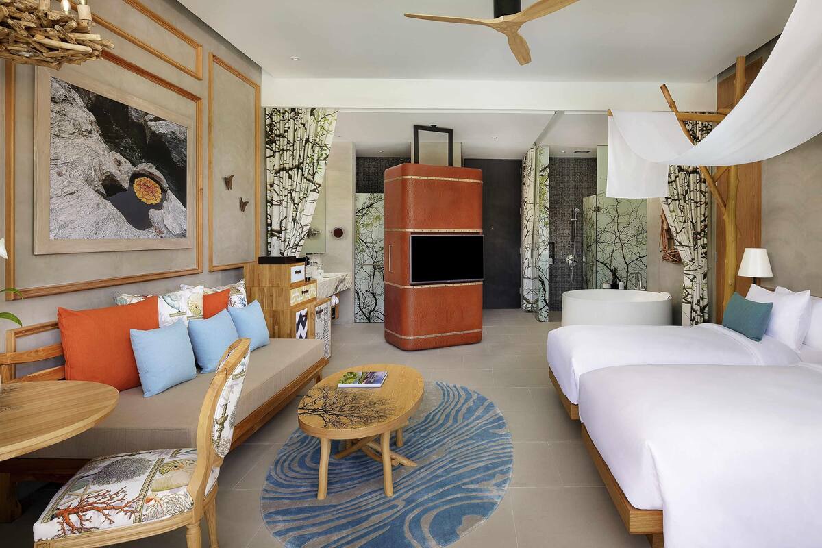 Een moderne hotelkamer met een bed, bank, eettafel en plafondventilator.