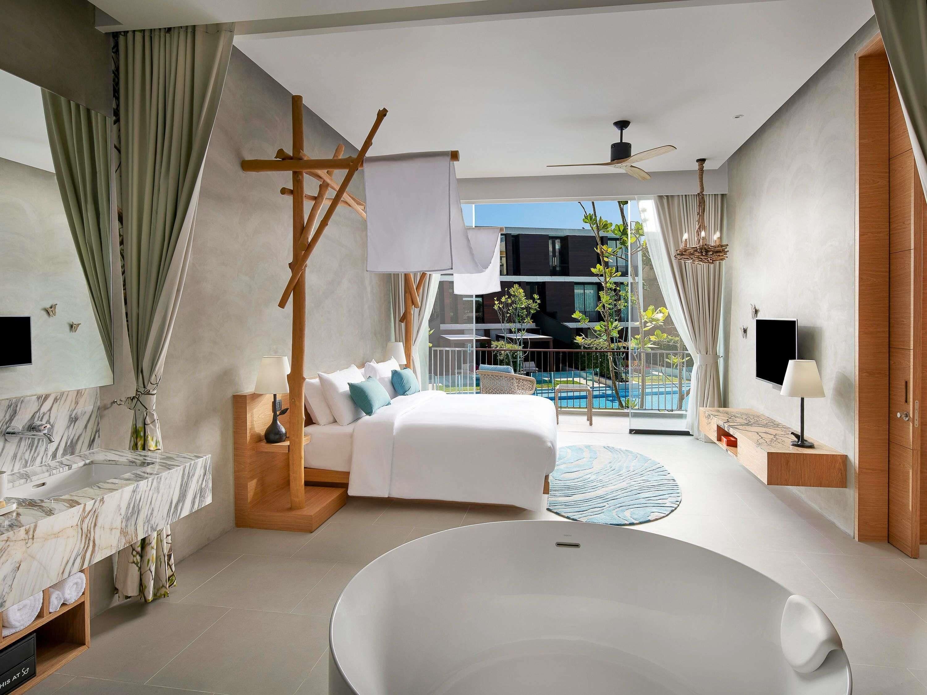 A modern hotel room with a large bed, a bathtub, a balcony with a pool, and a TV.