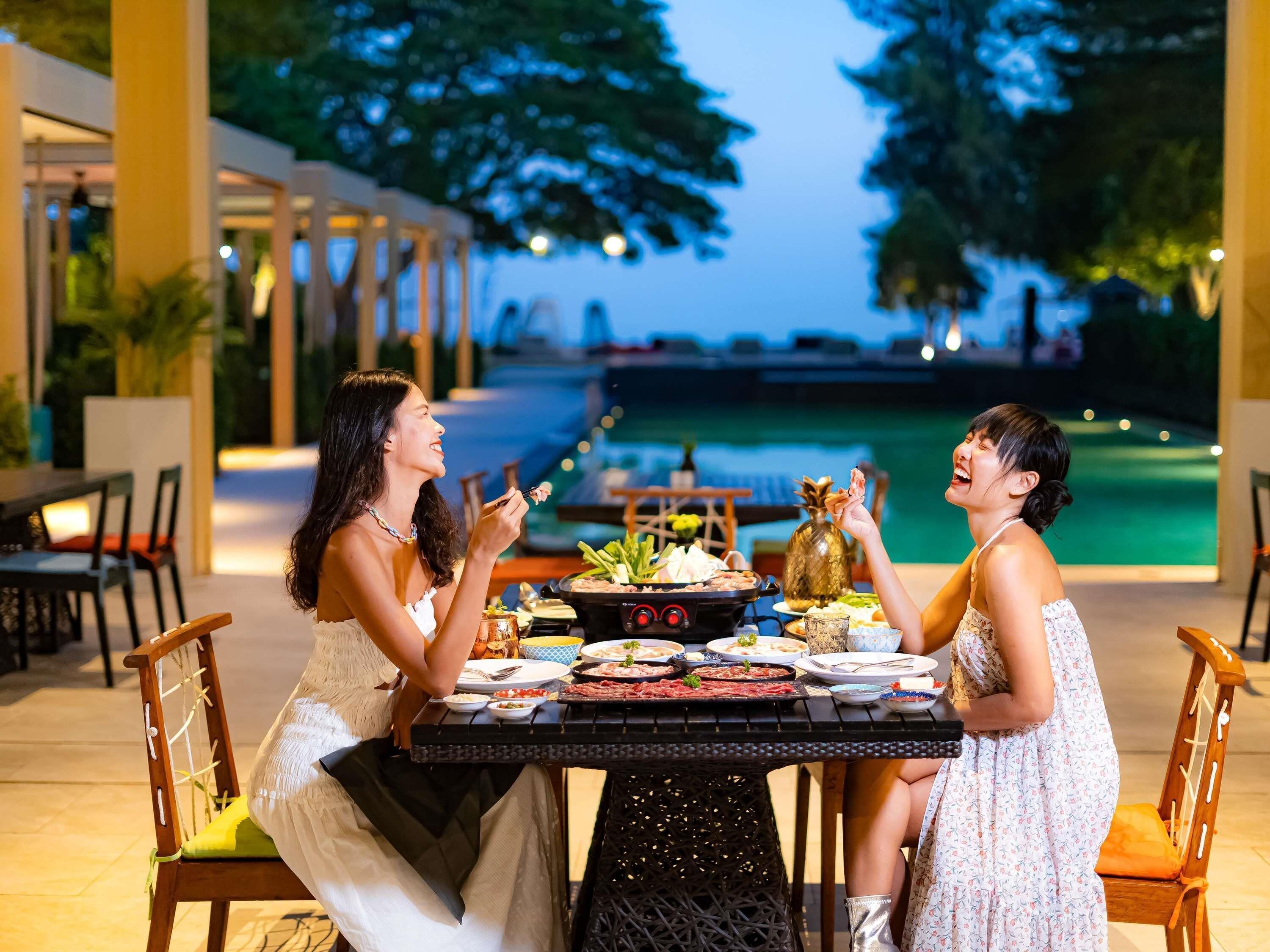 An outdoor dining area with a pool view, a grill, and a table set for two.