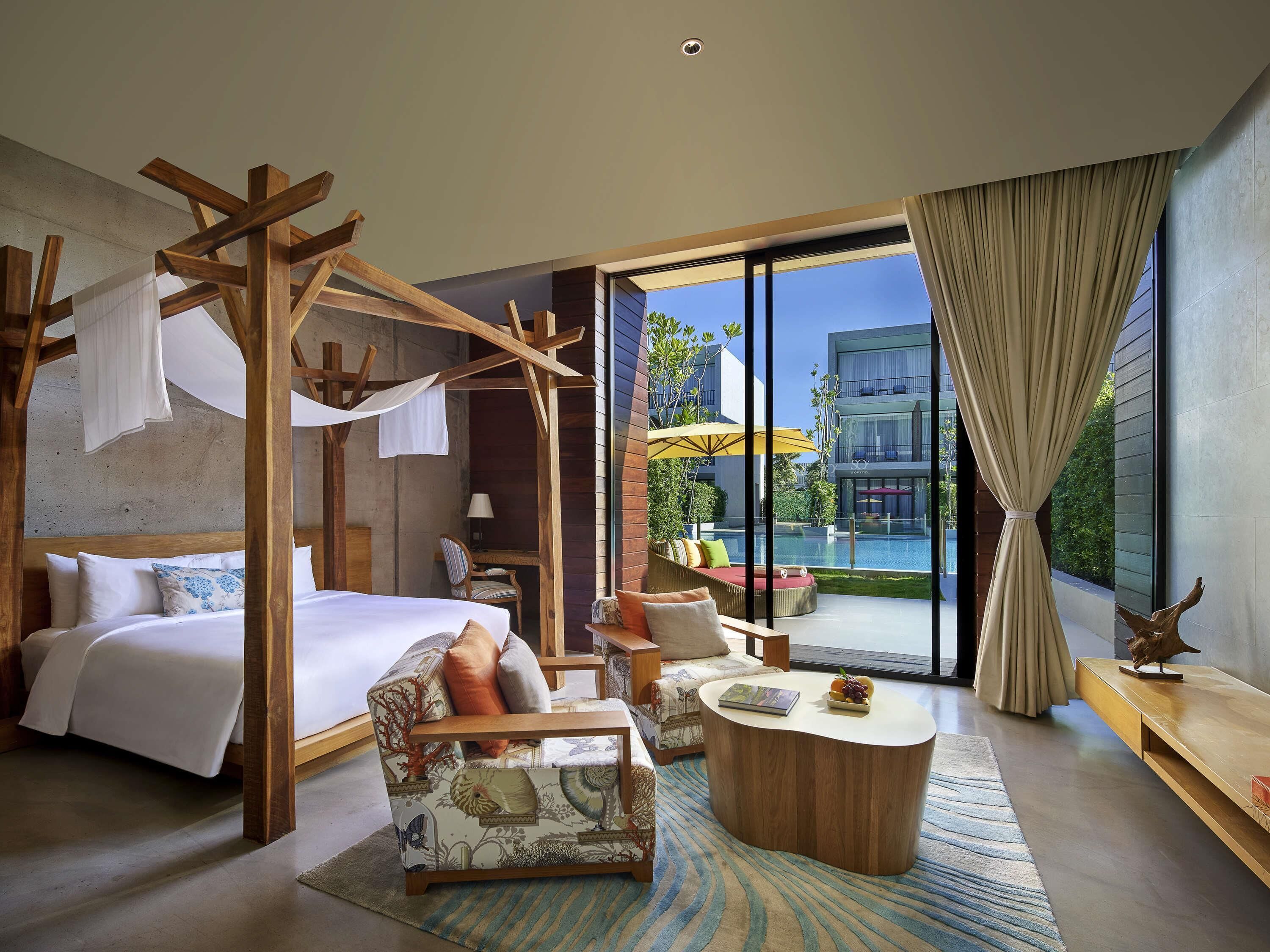 A bedroom with a canopy bed, a sitting area with a coffee table, and a view of a swimming pool.