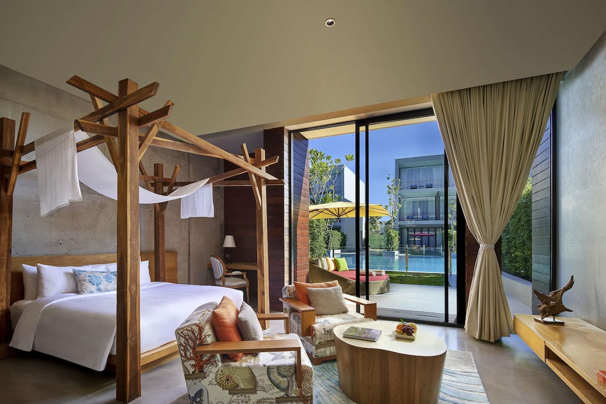 A bedroom with a canopy bed, a sitting area with a coffee table, and a view of a swimming pool.
